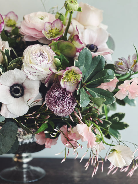 Event centerpiece in silver footed bowl in soft tones including anemones, helleborus, jasmine, sweetpea, frittilaria, and ranunculus.