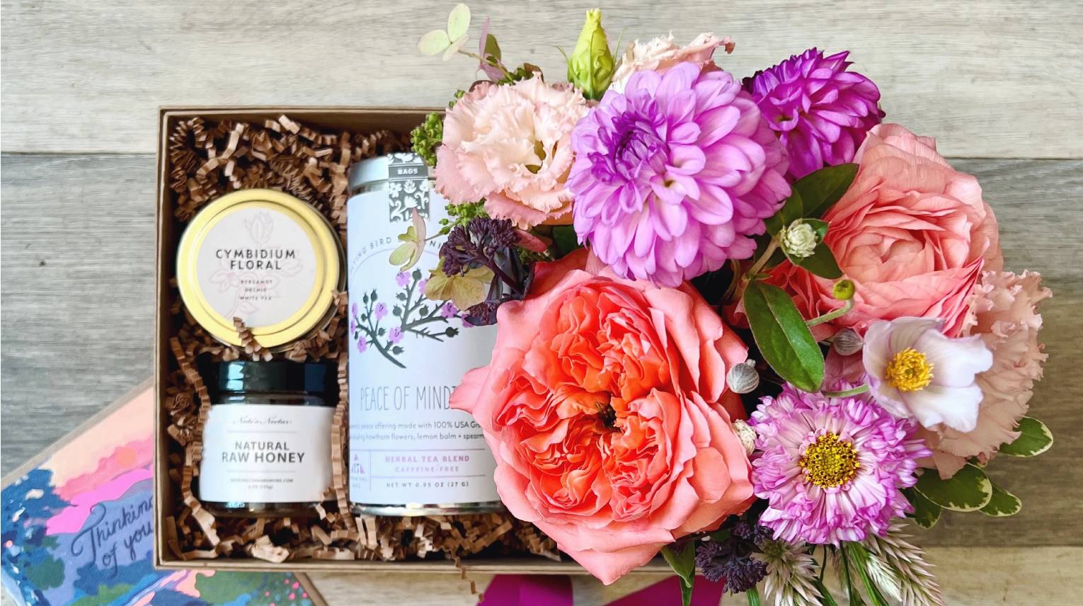 Condolence flower arrangement in a kraft gift box with tea, honey, and a candle.