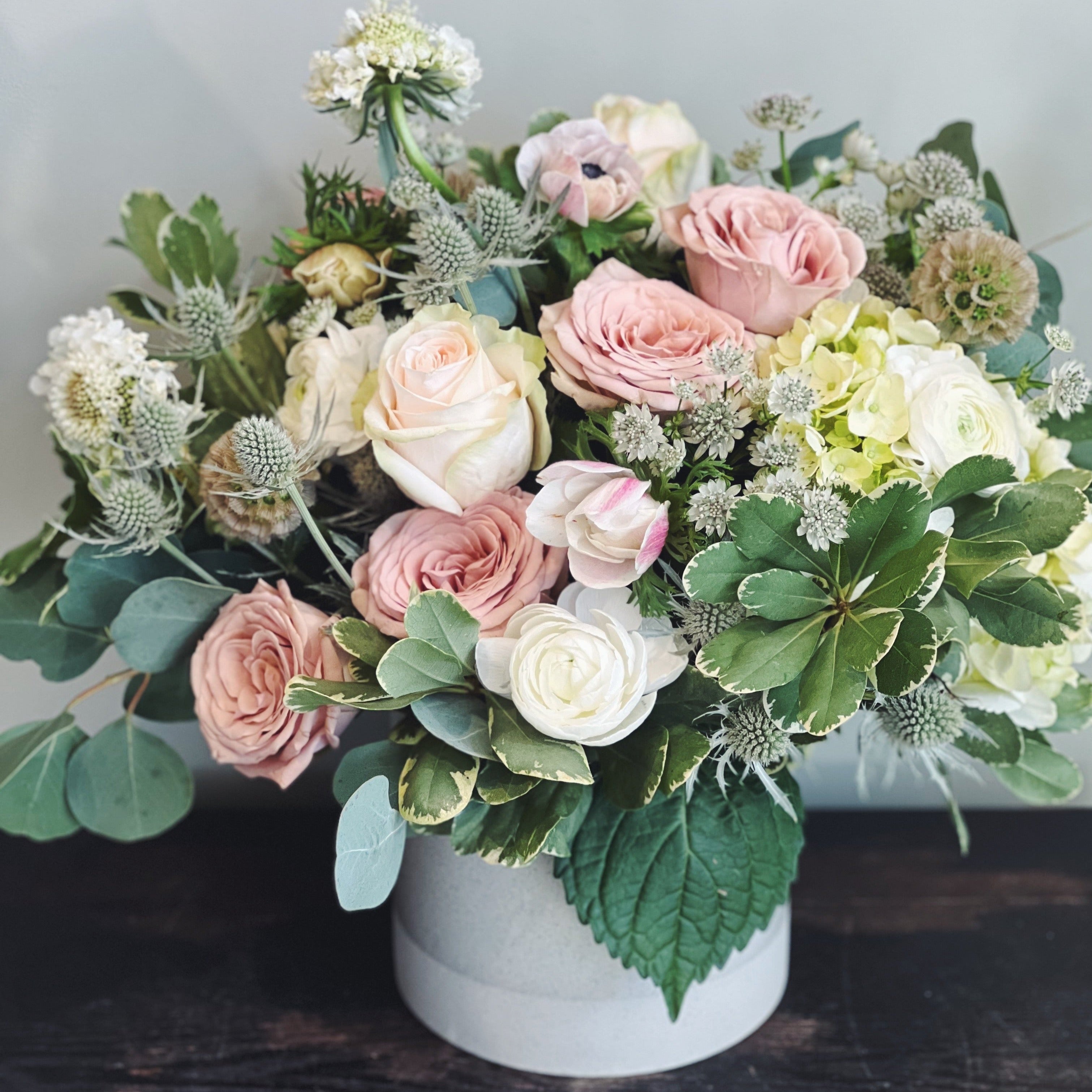 Soft sympathy or condolence flowers in blush, cream and green with roses and ranunculus in a ceramic vase. 