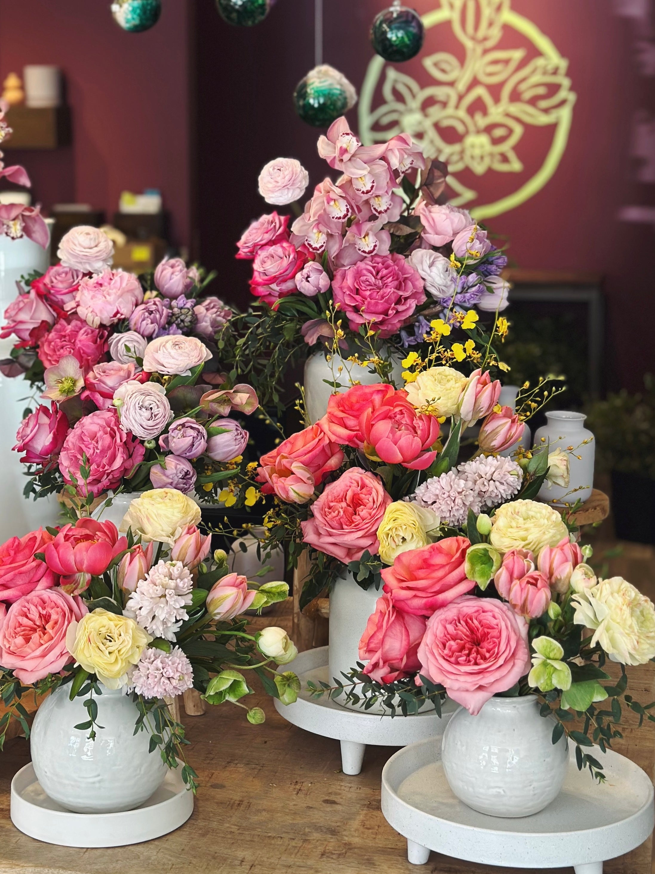 Six flower arrangements displayed on a wood table in the flower shop.  