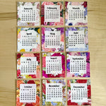 Grid of monthly calendars with floral designs on a wooden surface