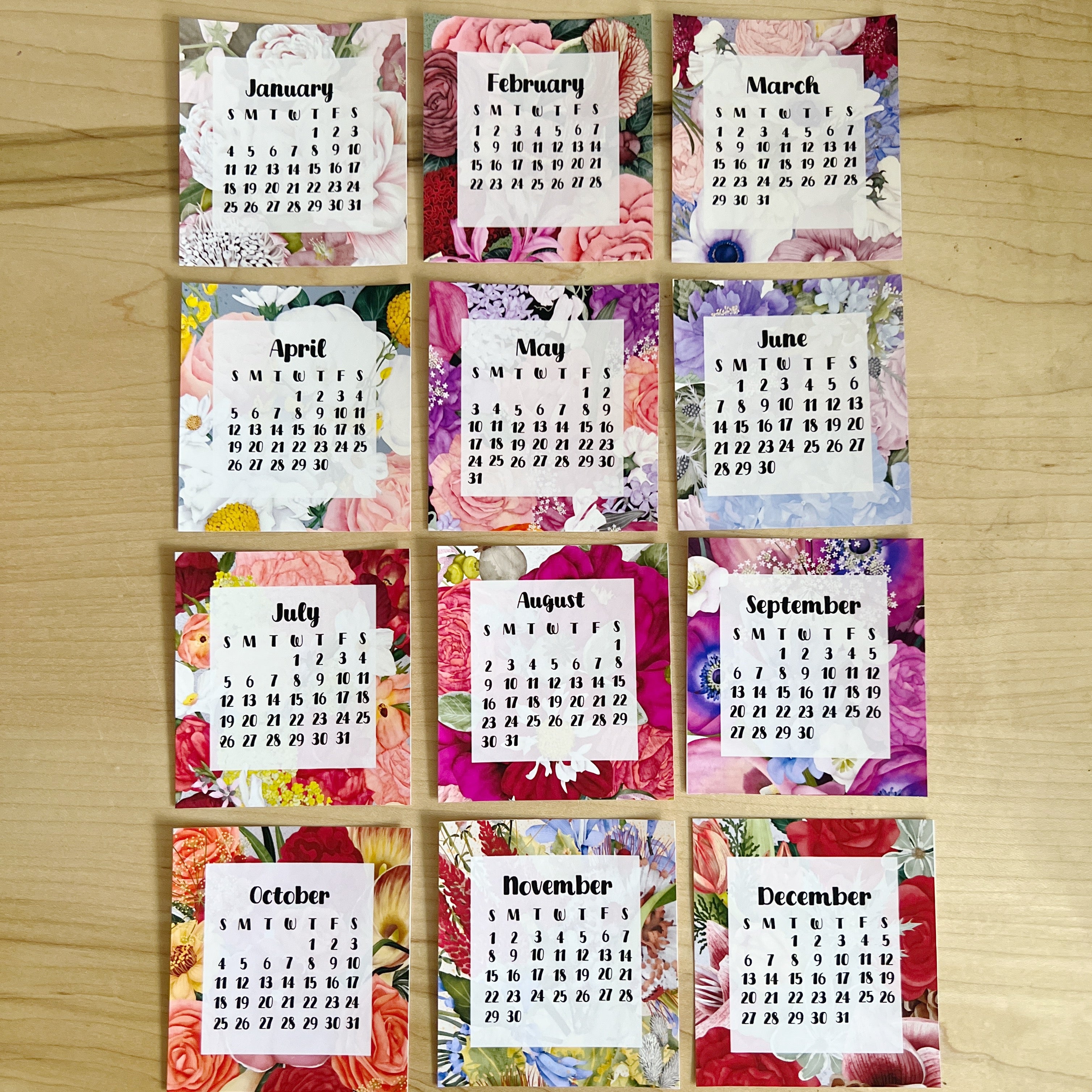 Grid of monthly calendars with floral designs on a wooden surface
