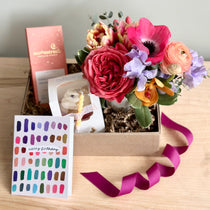 Gift box with flowers, a card, and a pink ribbon on a wooden surface.