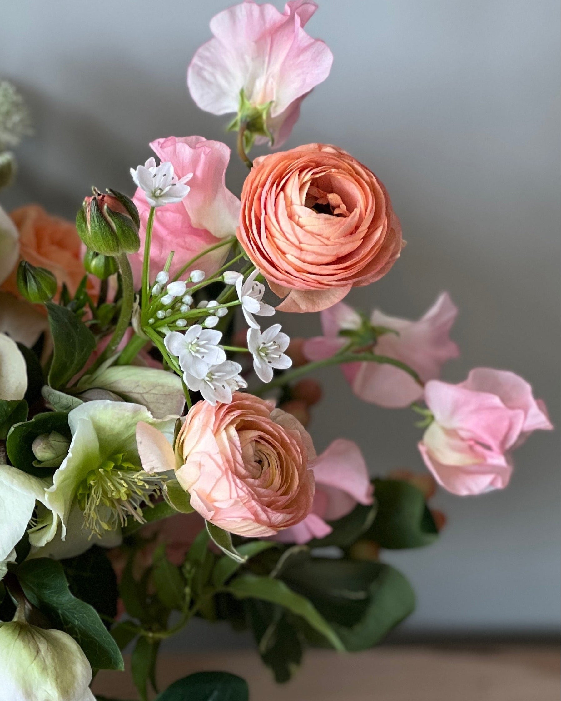 Bouquet of soft peach and white flowers in a white vase on a wooden surface with a light gray background
