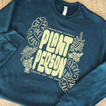 Deep green sweatshirt with 'Plant Person' text and floral designs on a wooden surface