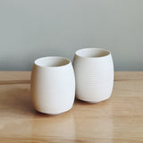 Two white porcelain teacups on a wooden surface with a gray background