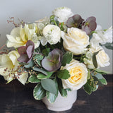 Large lush and low flower arrangement in white, cream, green, and stormy purple.  Roses, ranunculus, astrantia, helleborus, tulips. eucalyptus.