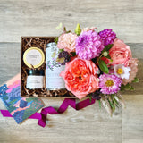 A sympathy or condolence themed gift box or basket  with flowers, candle, tea, honey and a card on a wooden surface