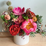 Colorful flower arrangement with a peony, orchids, roses and amaryllis in a white vase on a wooden surface with a light gray background