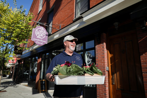 Photo of delivery driver carrying a tray of flower deliveries outside of Cymbidium Floral.
