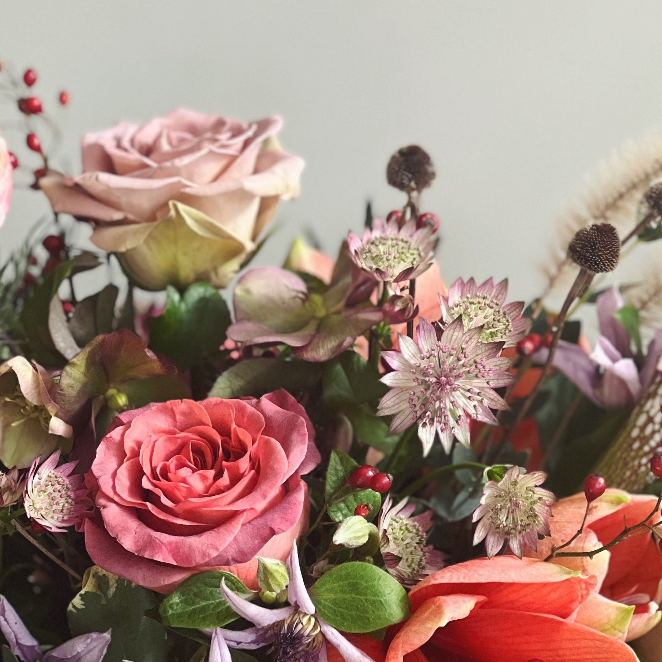 Bouquet of colorful autumn flowers with pink, red, and green tones against a light gray background.