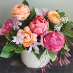 Lush and low flower arrangement in peahc, coral, and lavender.  Roses, peony french tulips, muscari, clematis, ranunculus, jasmine.