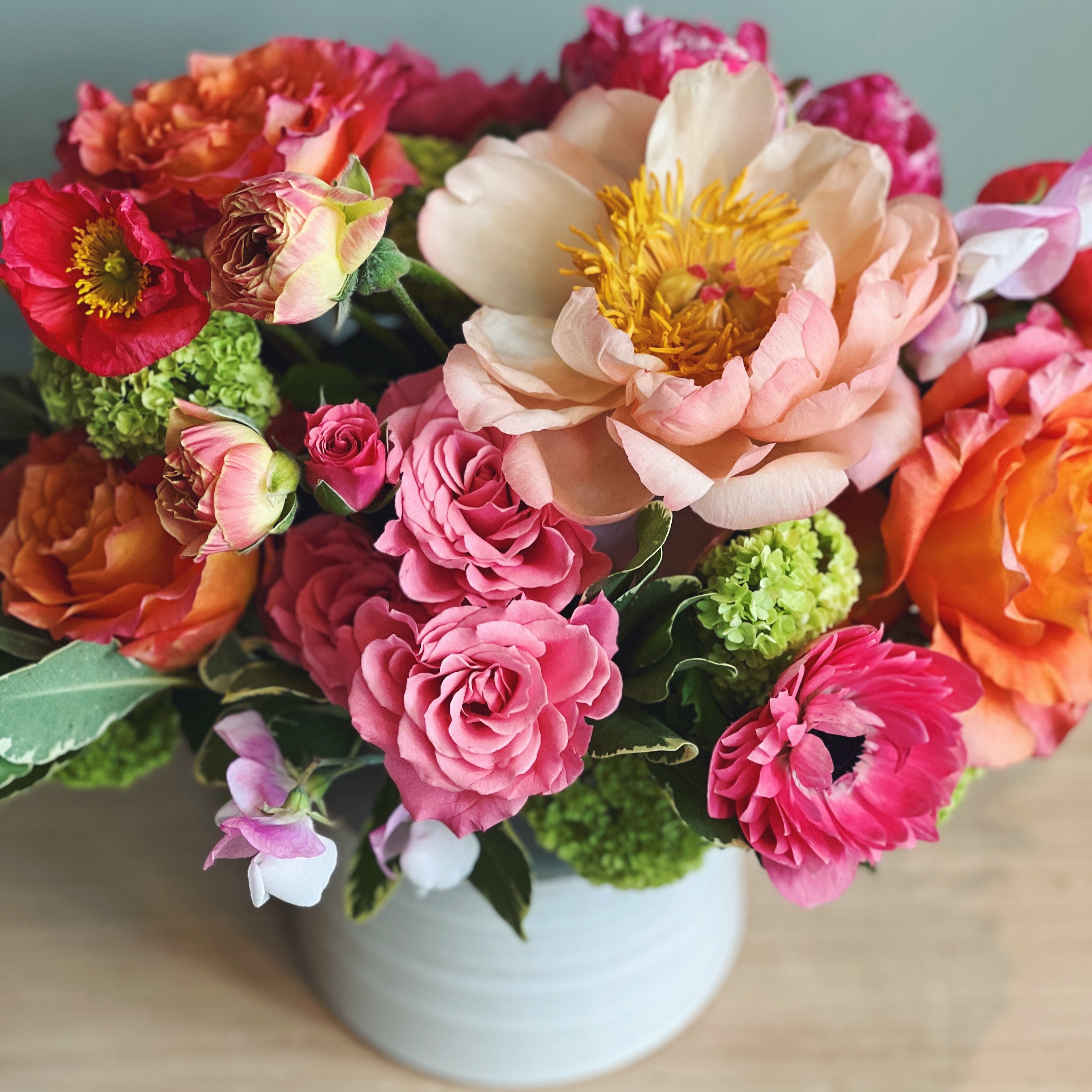 Bouquet of high-end colorful flowers with peonies, roses, poppies and anemones in a white vase on a wooden surface