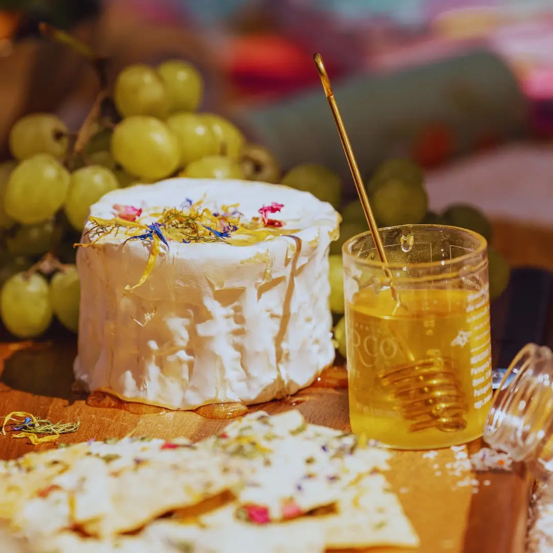 Cheese platter garnished with edible flowers with crackers, honey, and grapes on a wooden board.