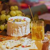 Cheese platter garnished with edible flowers with crackers, honey, and grapes on a wooden board.