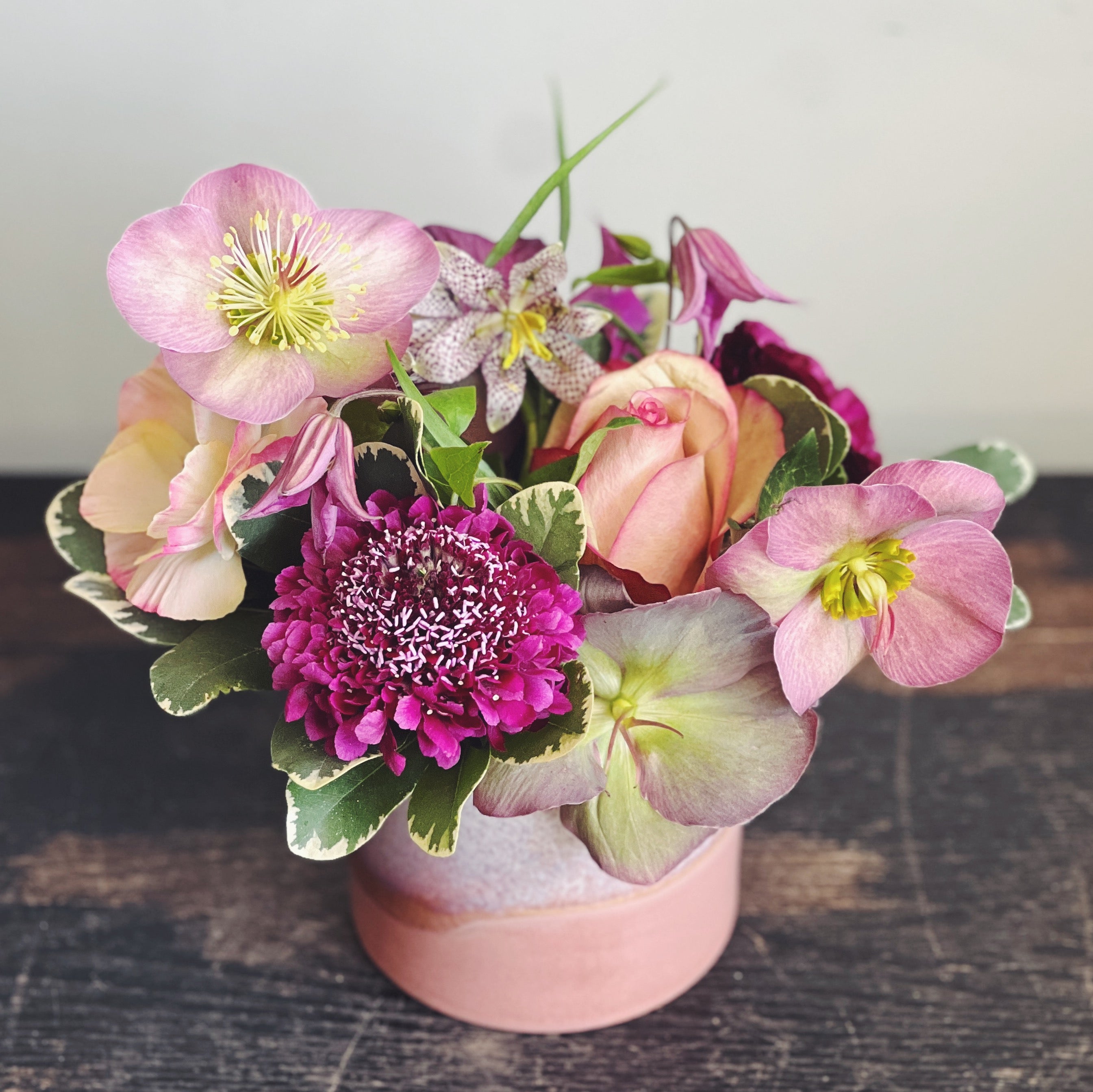 Small arrangement in a terracotta colored vase.  Flowers in mauve, plum, and burgundy.  Scabiosa, helleborus, roses, frittilaria, clematis. 