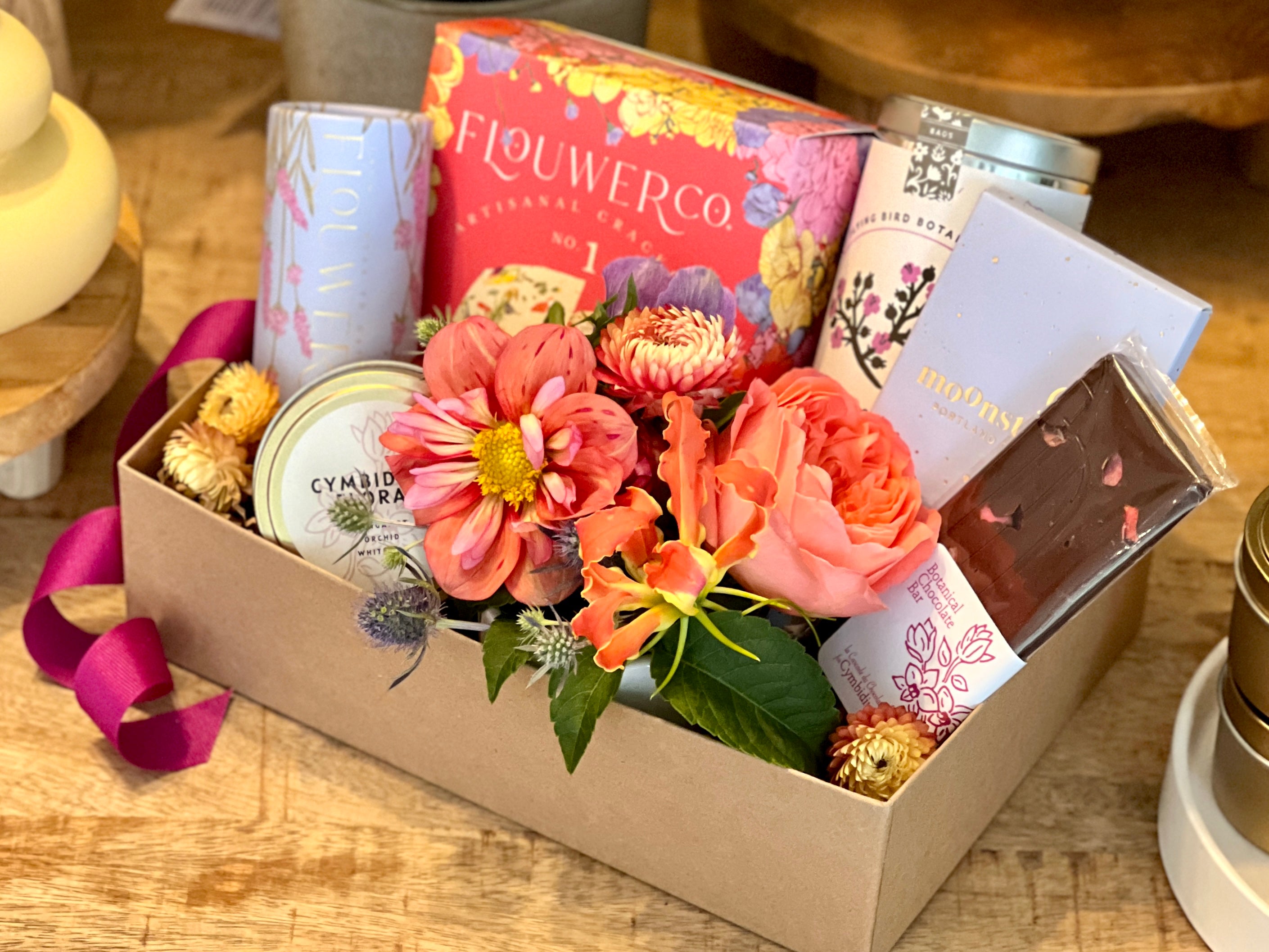 Gift box or basket with premium flowers, gourmet crackers, organic tea, chocolate bars, candle, and floral cocktail cubes.