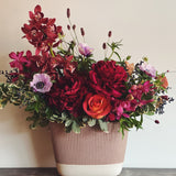 Burgundy, magenta, lavender, and deep red holiday luxe flower arrangement in a beige oval ceramic vase.  Orchids, anemones, peonies, roses, sanguisorba, and privet berries.