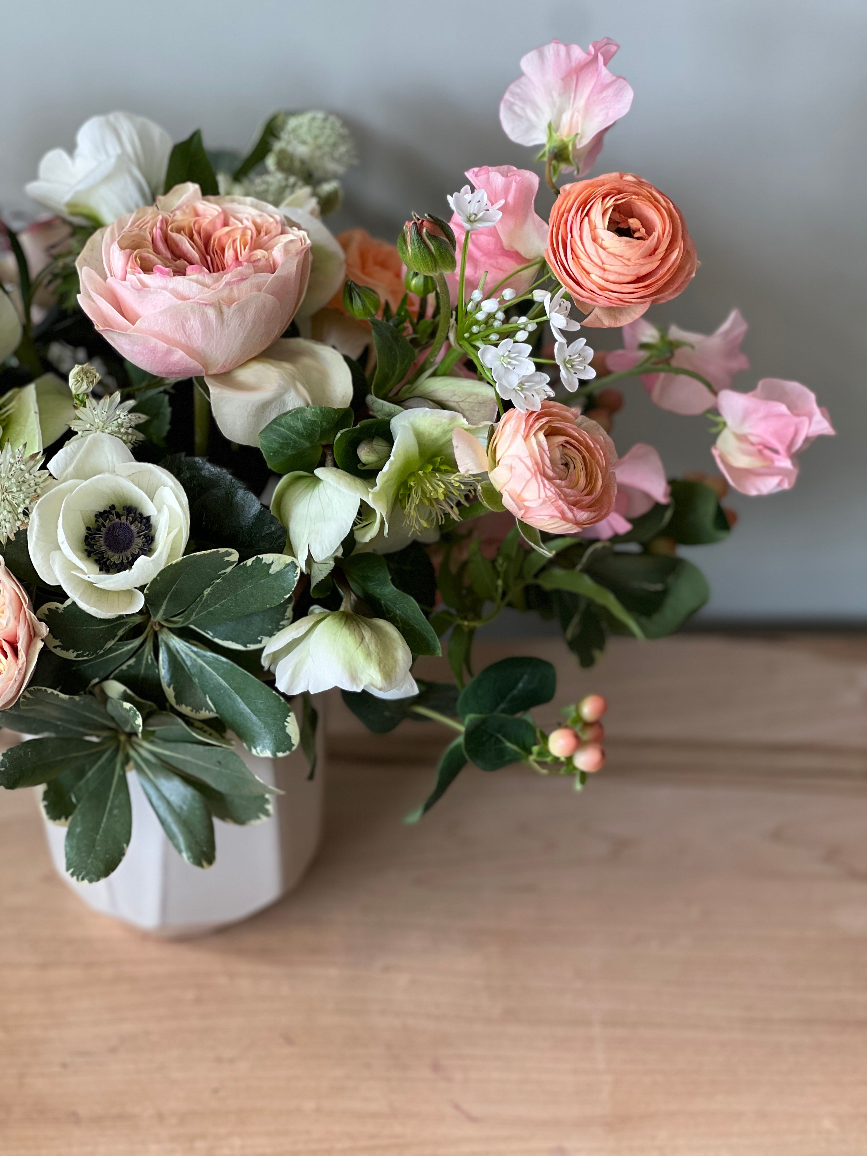 Flower arrangement featuring premium flowers like white anemones, peach ranunculus, sweet pea, hellebores and roses. 