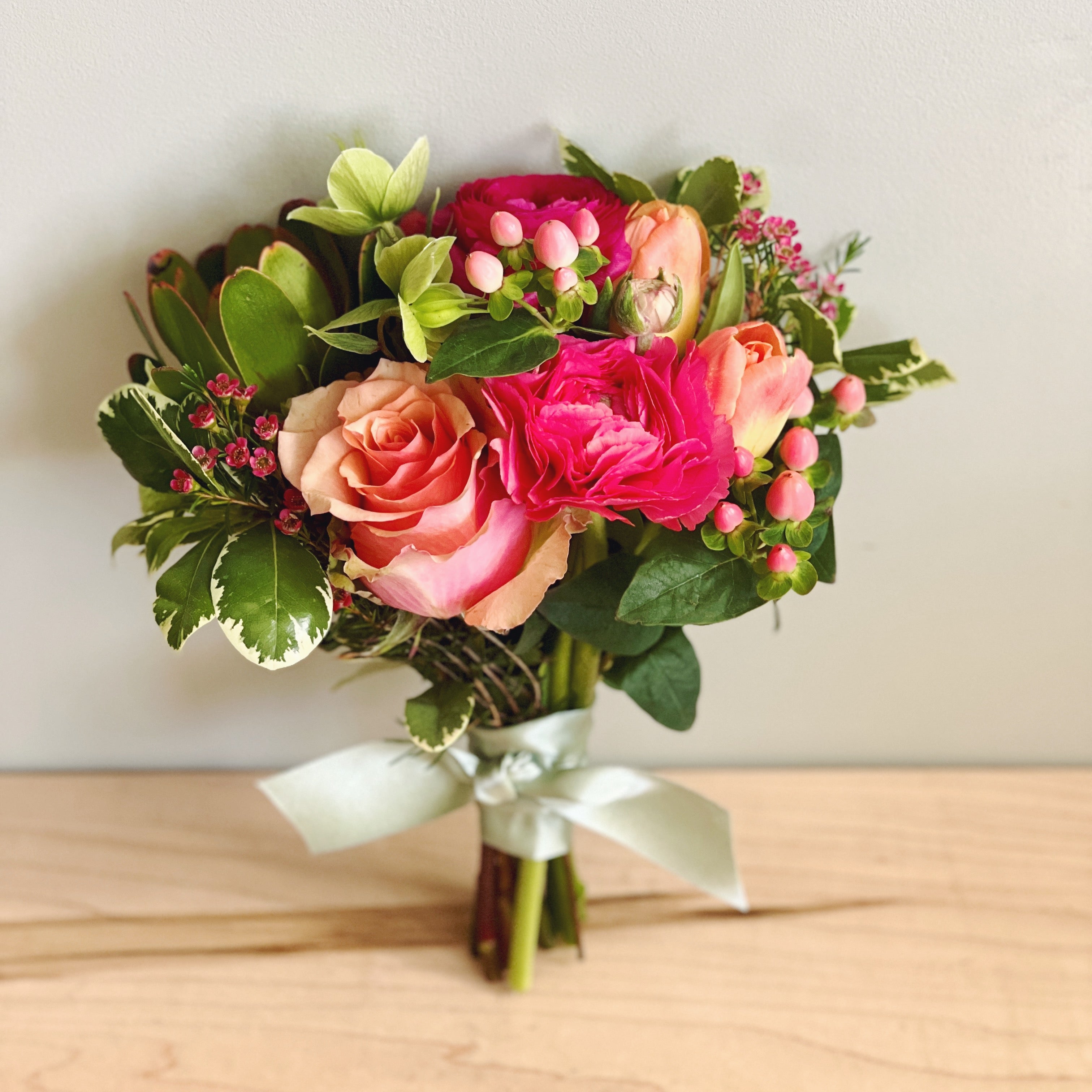 Handheld prom bouquet of coral and hot pink flowers wrapped with ribbon. 