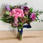 Handheld prom bouquet of pink and purple flowers wrapped with ribbon. 