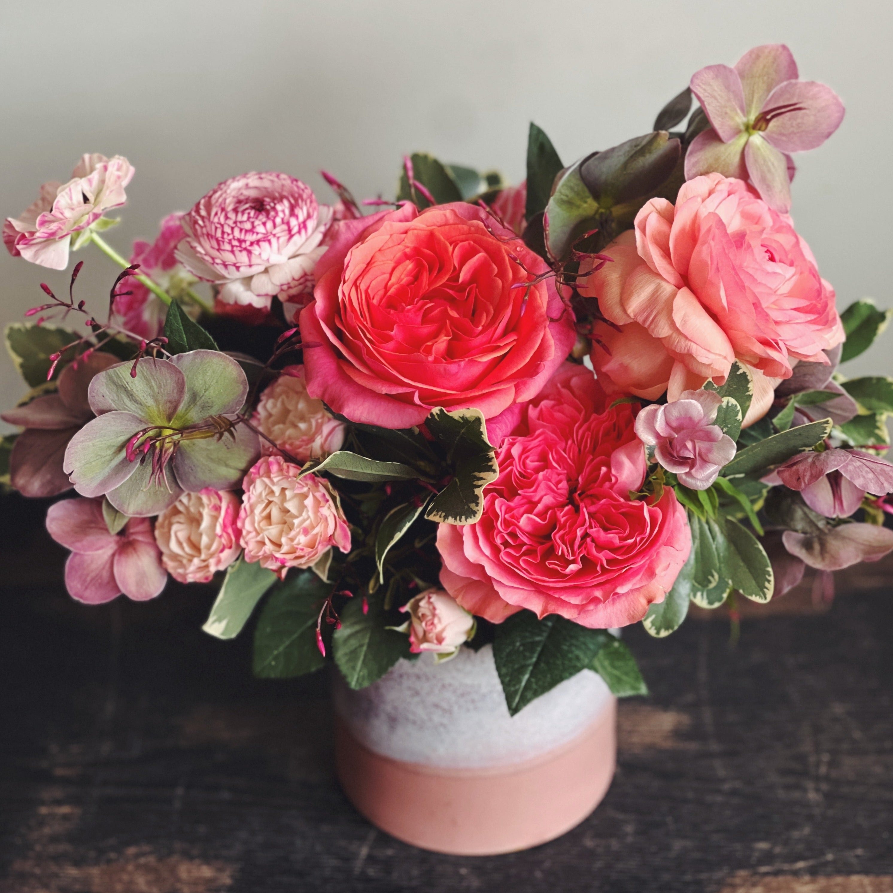 Flower arrangement in a terracotta colored vase with flowers in hot pink, mauve, and cream.  Spray roses, ranunculus, roses, helleborus.