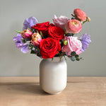 Unique Valentine's Day flowers in a ceramic vase featuring roses, ranunculus, tulips, and sweetpea in shades of pinks, red and lavender. 