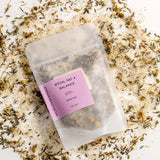 Tea package labeled 'Ritual No. 4 Balance' on a bed of dried herbs.