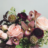 A floral arrangement featuring roses and orchids in shades of peach and burgundy, with green foliage.
