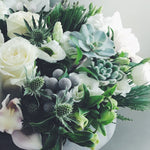 Holiday flower arrangement in white, grey, and green.  Flowers include: roses, cymbidium orchids, thistle, succulents, helleborus, and evergreens. 