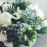 Holiday flower arrangement in white, grey, and green.  Flowers include: roses, cymbidium orchids, thistle, succulents, helleborus, and evergreens. 