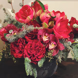 Holiday flower arrangement in reds and burgundy with evergreens roses, cymbidium orchids, amaryllis, and eucalyptus. 