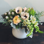 Holiday flower arrangement in white, grey, cream and green.  Flowers include: ranunculus, anemone, star of bethlehem, silver berzelia, and evergreens.