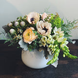Holiday flower arrangement in white, grey, cream and green.  Flowers include: ranunculus, anemone, star of bethlehem, silver berzelia, and evergreens.