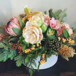 Holiday flower arrangement in pale pink, cream, green, and red. Flowers include: amaryllis, pink protea, lady slipper orchid, kale, pepperberry, and evergreens.