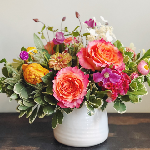 Bold and bright lush and low arrangement in orange, coral, fuschia, and peach.  Flowers include: roses, zinnias, ranunculus, clematis, strawflower, and thistle.