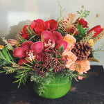 Holiday flower arrangement in burgundy, red, peach, and brown.  Flowers include: amaryllis, cymbidium orchids, roses, grevellia, pinecones and evergreens.