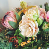 Holiday flower arrangement in pale pink, cream, green, and red.  Flowers include: amaryllis, pink protea, lady slipper orchid, kale, pepperberry, and evergreens. 