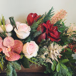 Holiday flower arrangement in pale pink, red, and peach.  Flowers include: amaryllis, grevellia, vanda orchids, astilbe, roses, pepperberry and evergreens.