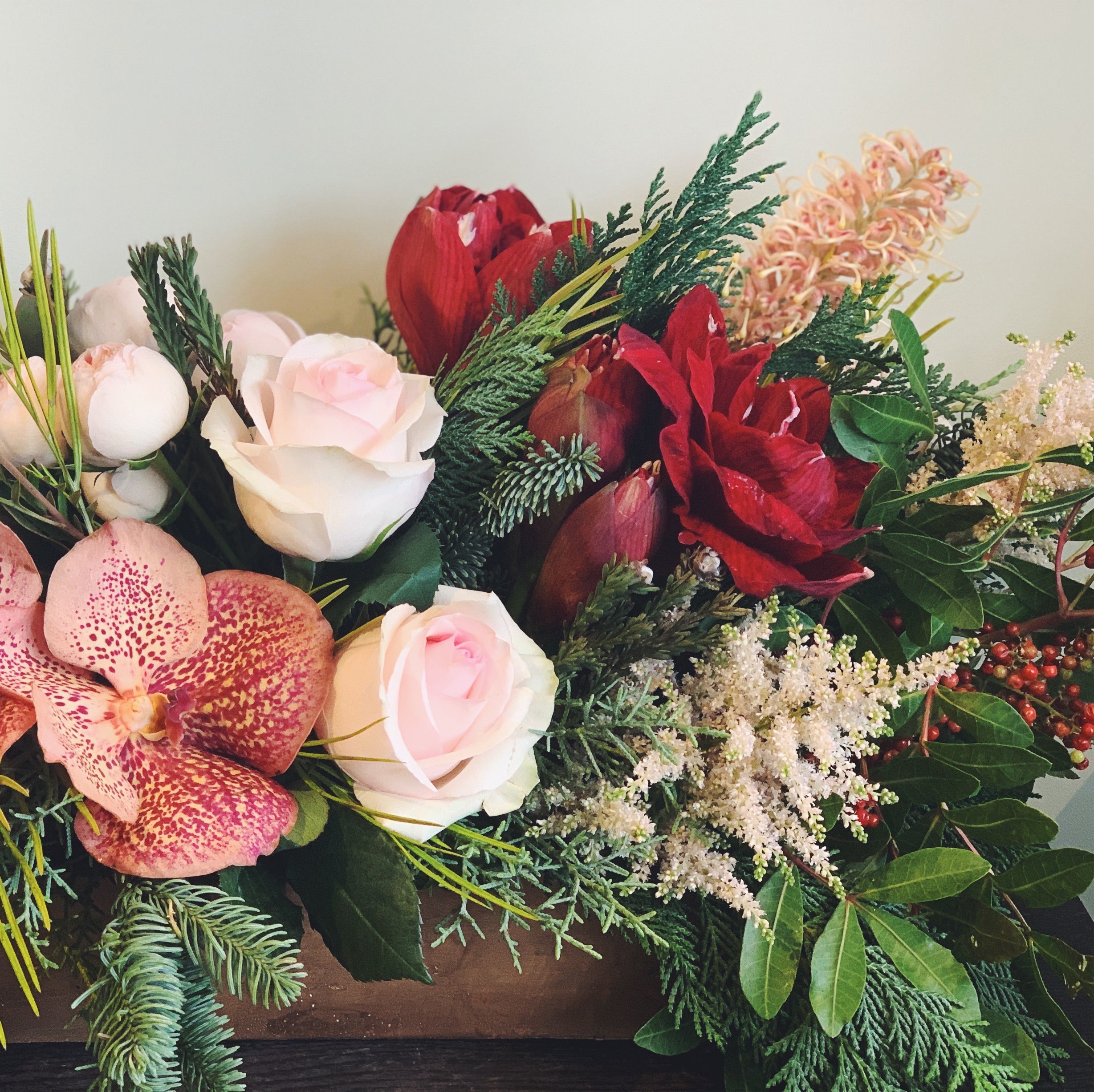 Holiday flower arrangement in pale pink, red, and peach.  Flowers include: amaryllis, grevellia, vanda orchids, astilbe, roses, pepperberry and evergreens.